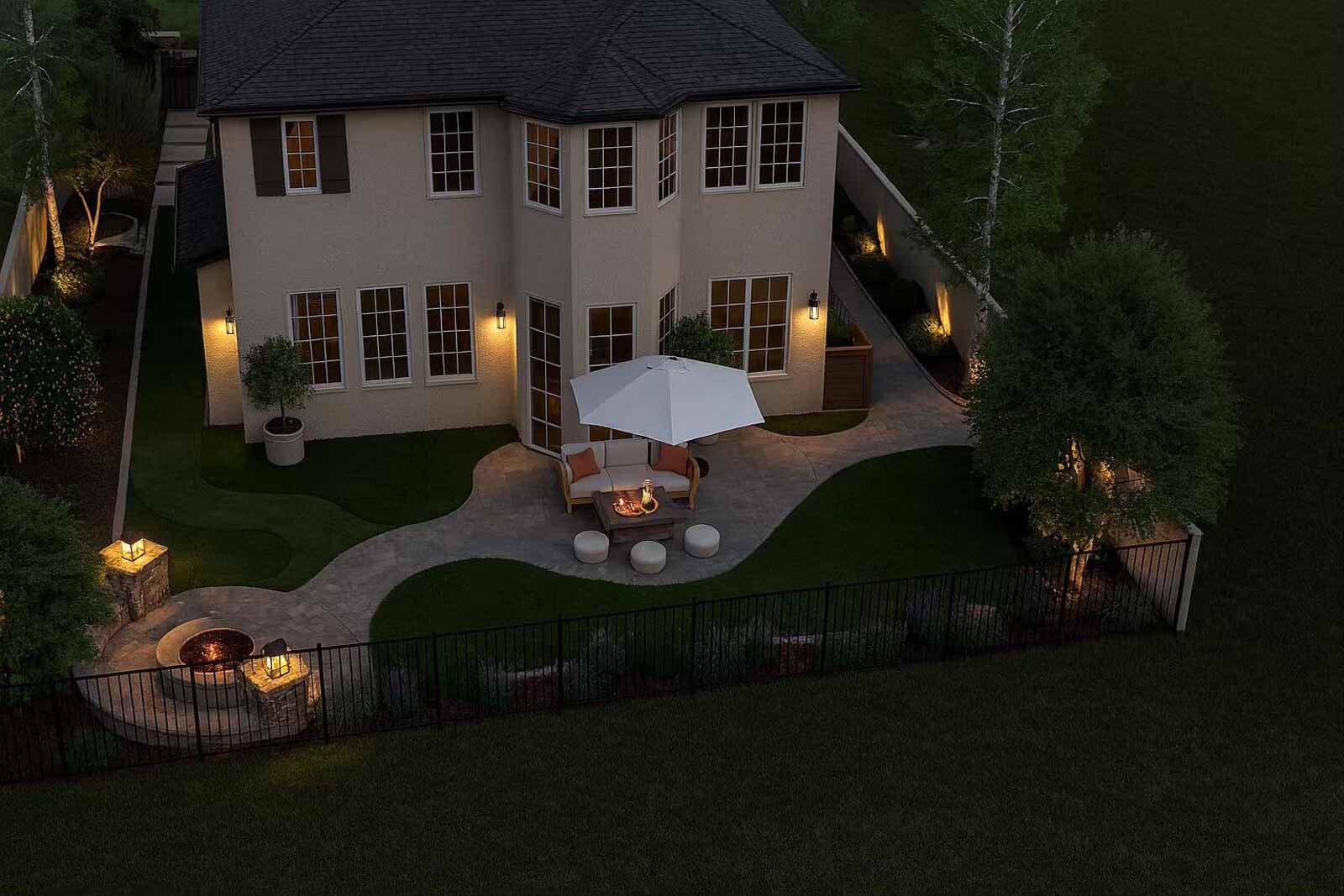 Aerial night view of backyard with organic paver patio, lounge seating, and landscape lighting