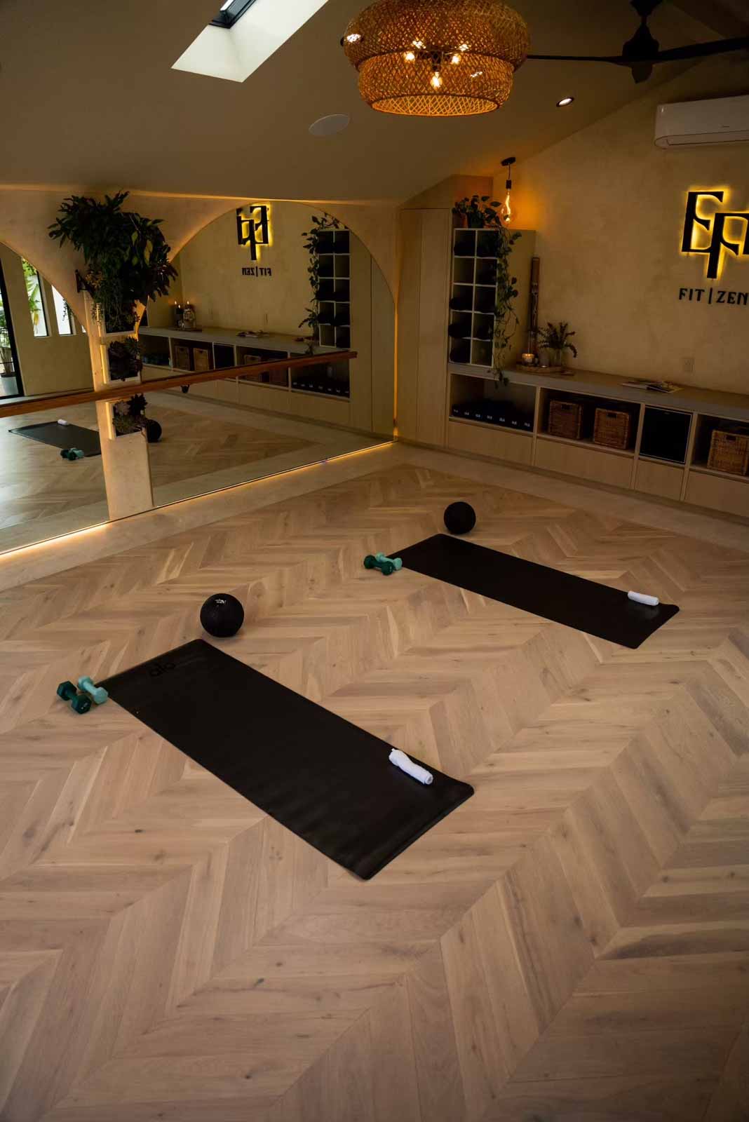 Yoga studio at dusk with warm lighting, mirrors, and herringbone flooring