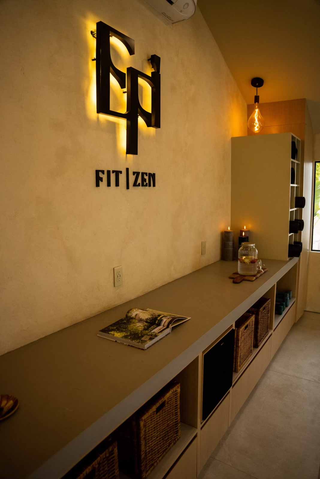 Close-up of backlit FIT ZEN logo on textured wall with storage below