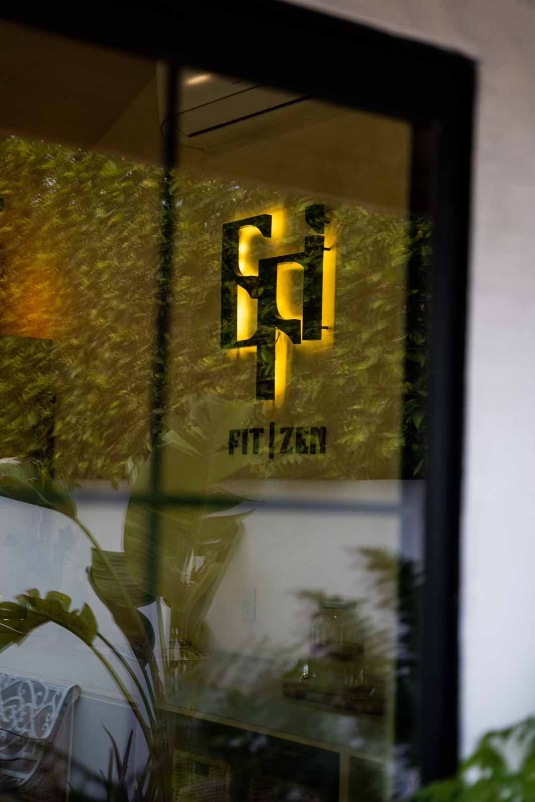 Illuminated FIT ZEN logo visible through window with greenery