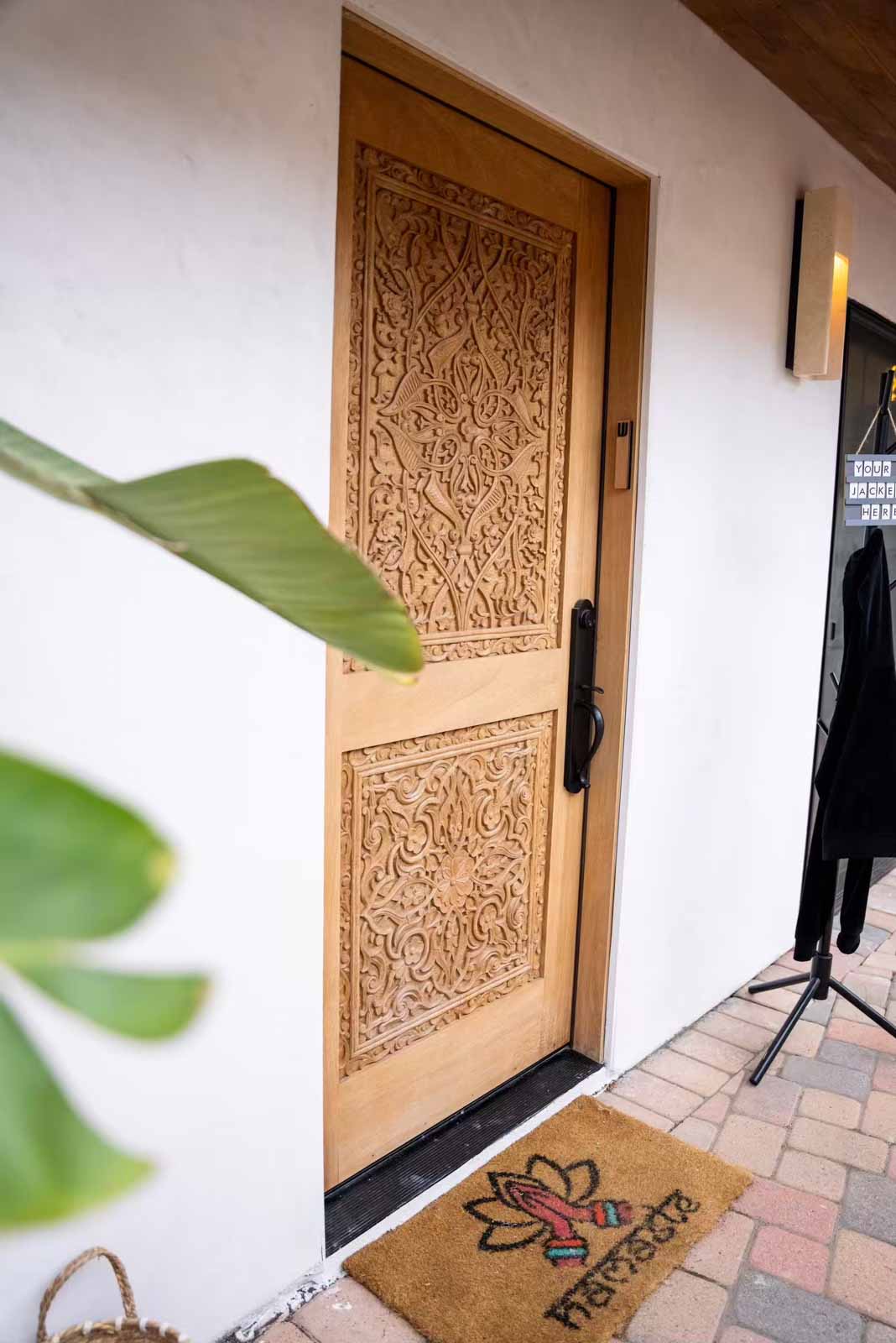 Ornate carved wood door with Namaste doormat and banana plant