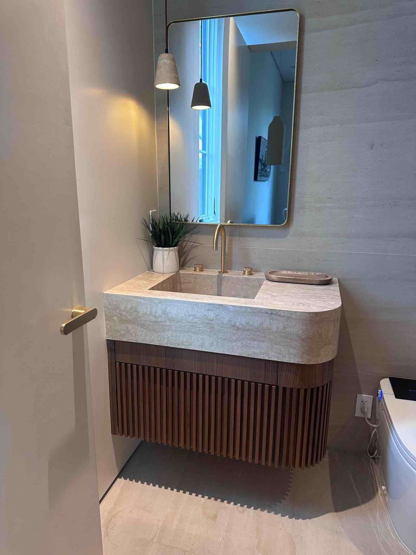 Encino ADU powder room with integrated travertine sink, fluted walnut vanity, brass faucet, and concrete pendant