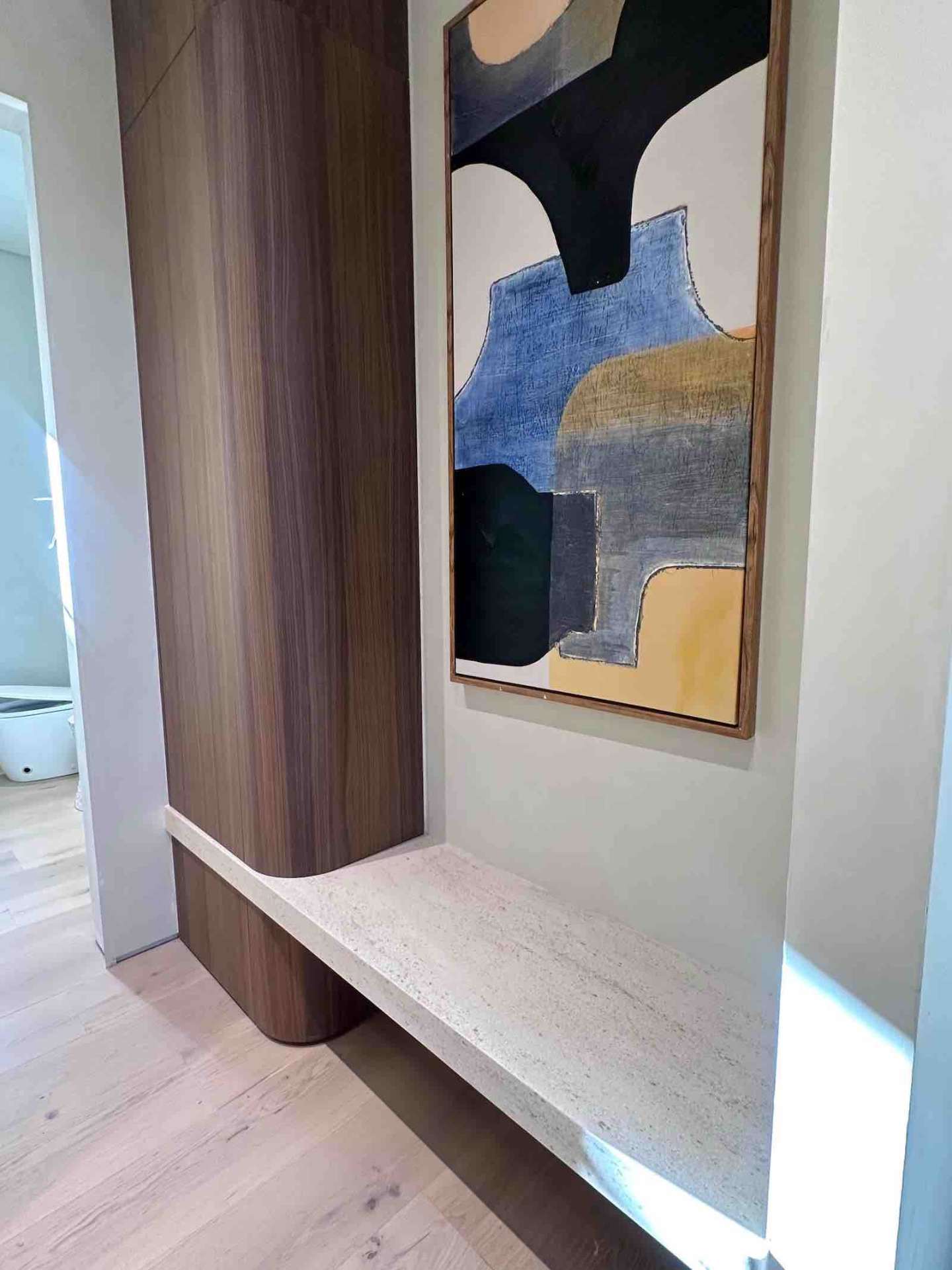 Encino ADU entryway with walnut millwork, floating stone bench, and abstract art