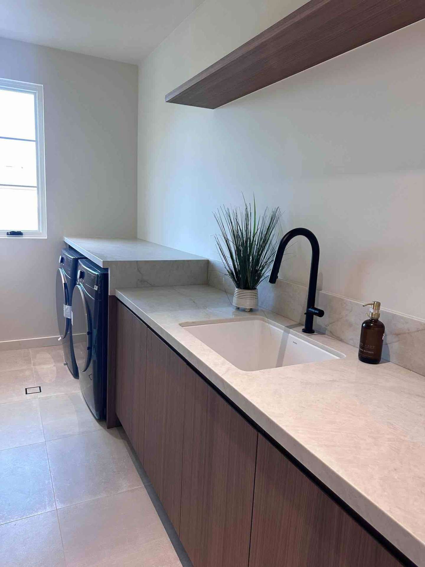 Encino ADU laundry room with quartz countertops, matte black faucet, walnut cabinets, and front-load washer dryer