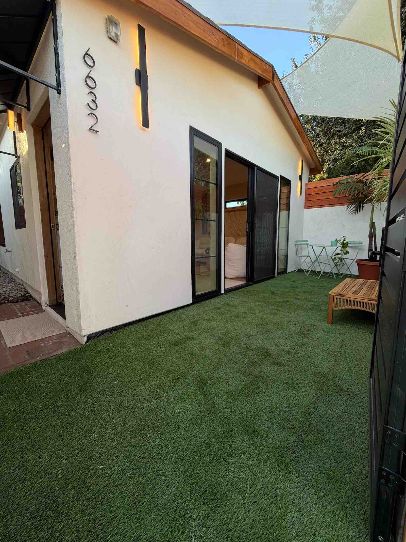 Fulton ADU exterior with private turf courtyard, black-framed sliding glass doors, vaulted wood beam, and modern white stucco facade