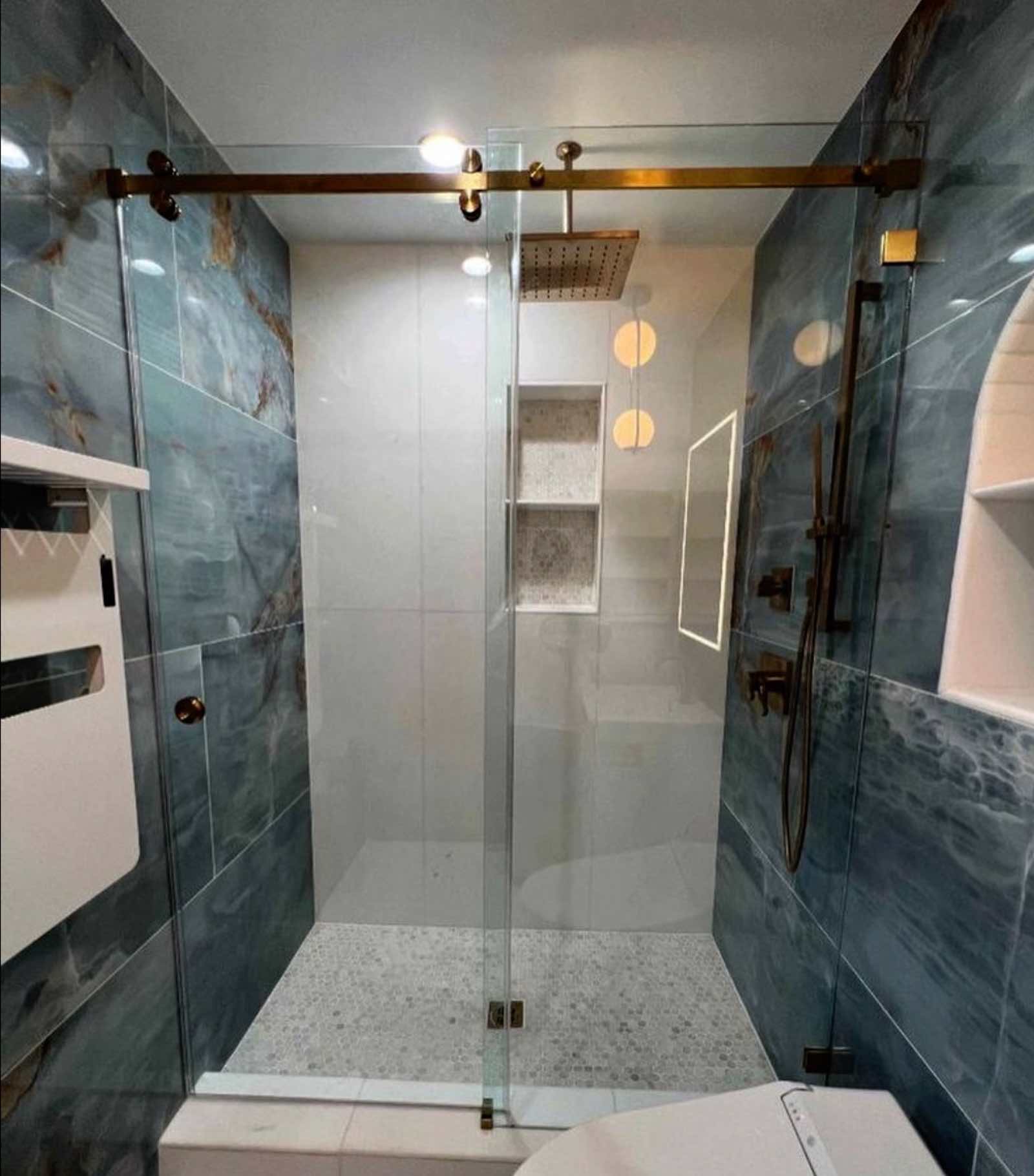 Alhambra walk-in shower with brass sliding glass door, rain showerhead, and hexagon floor tile