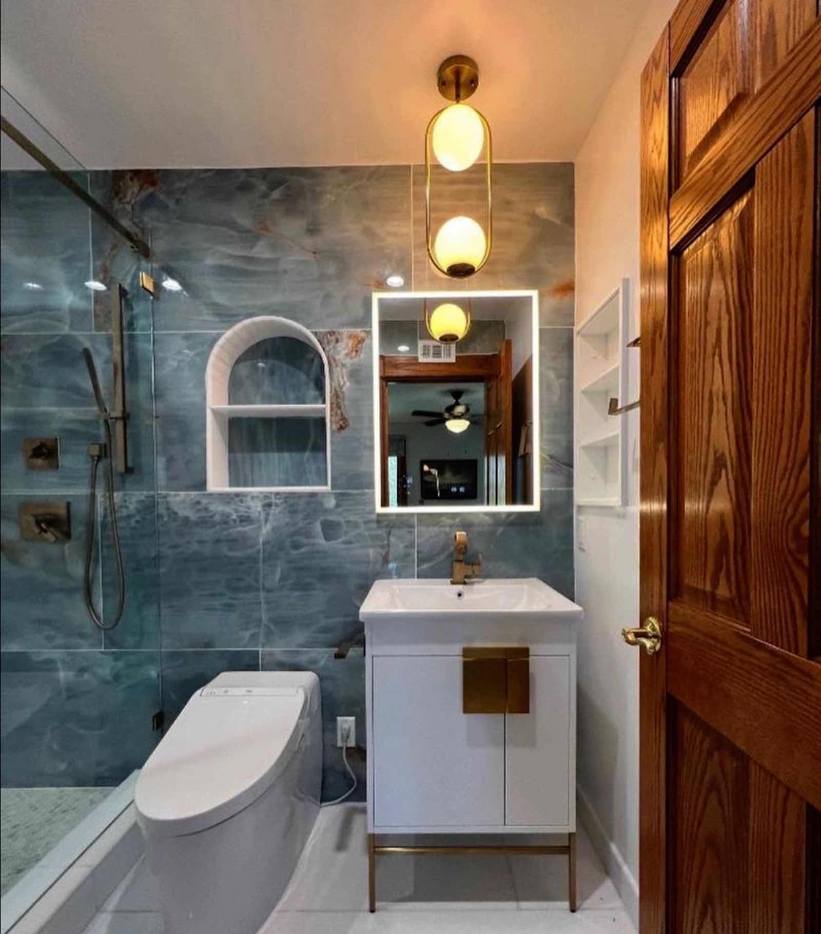 Alhambra bathroom with blue onyx tile wall, LED mirror, brass pendant, and floating vanity
