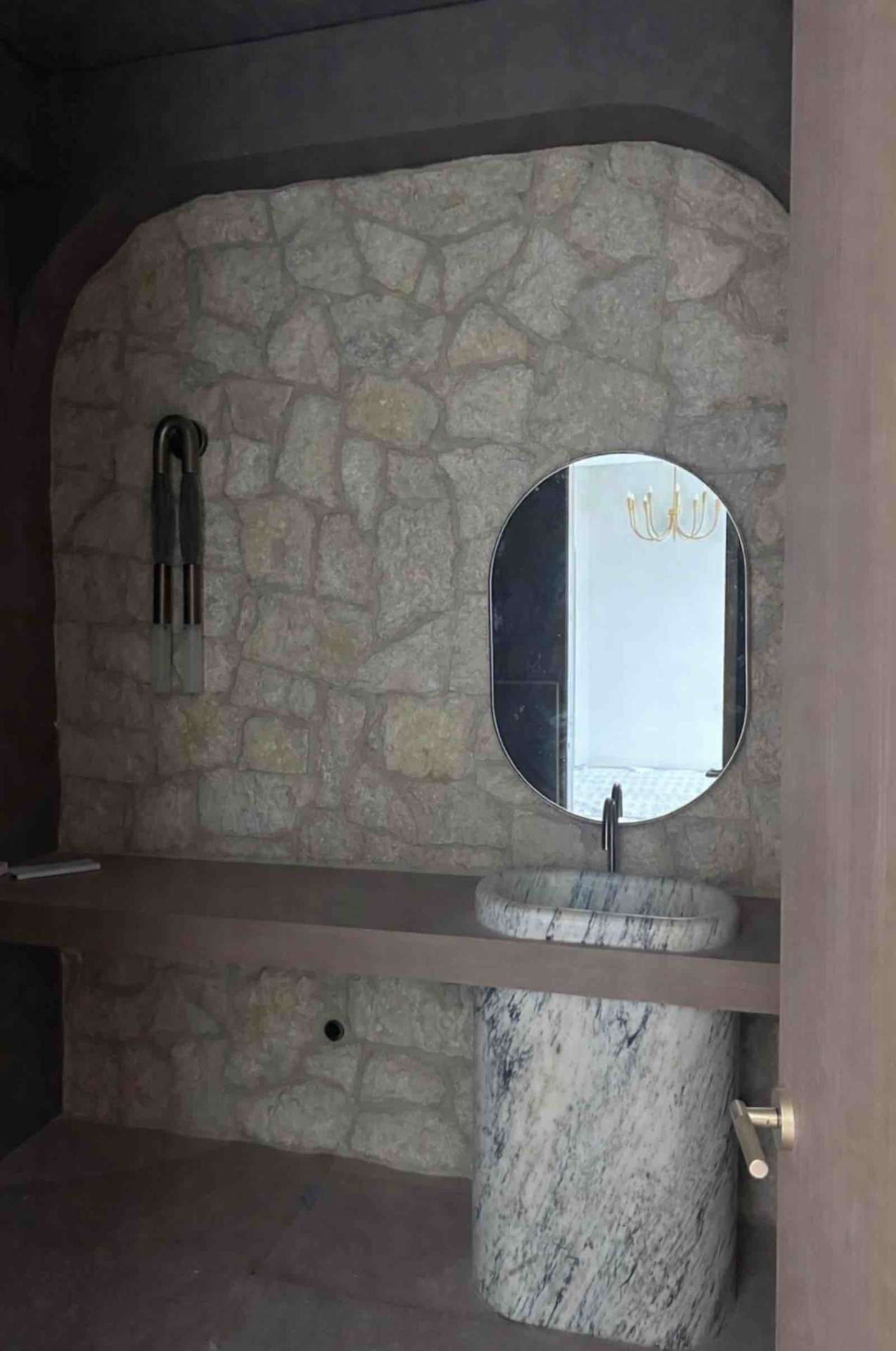 Encino powder room with flagstone accent wall, sculptural marble pedestal sink, and oval mirror