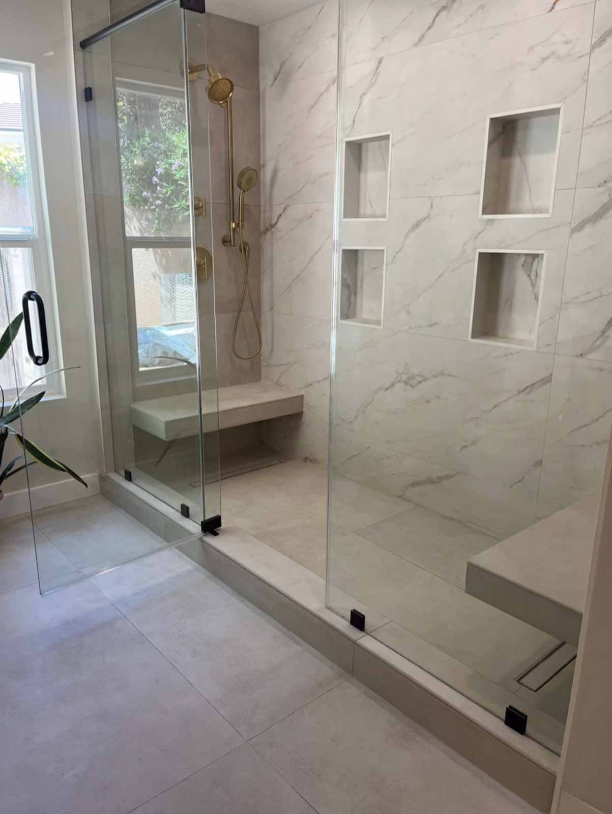 Large walk-in shower with glass enclosure, marble walls, and built-in niches - Los Angeles