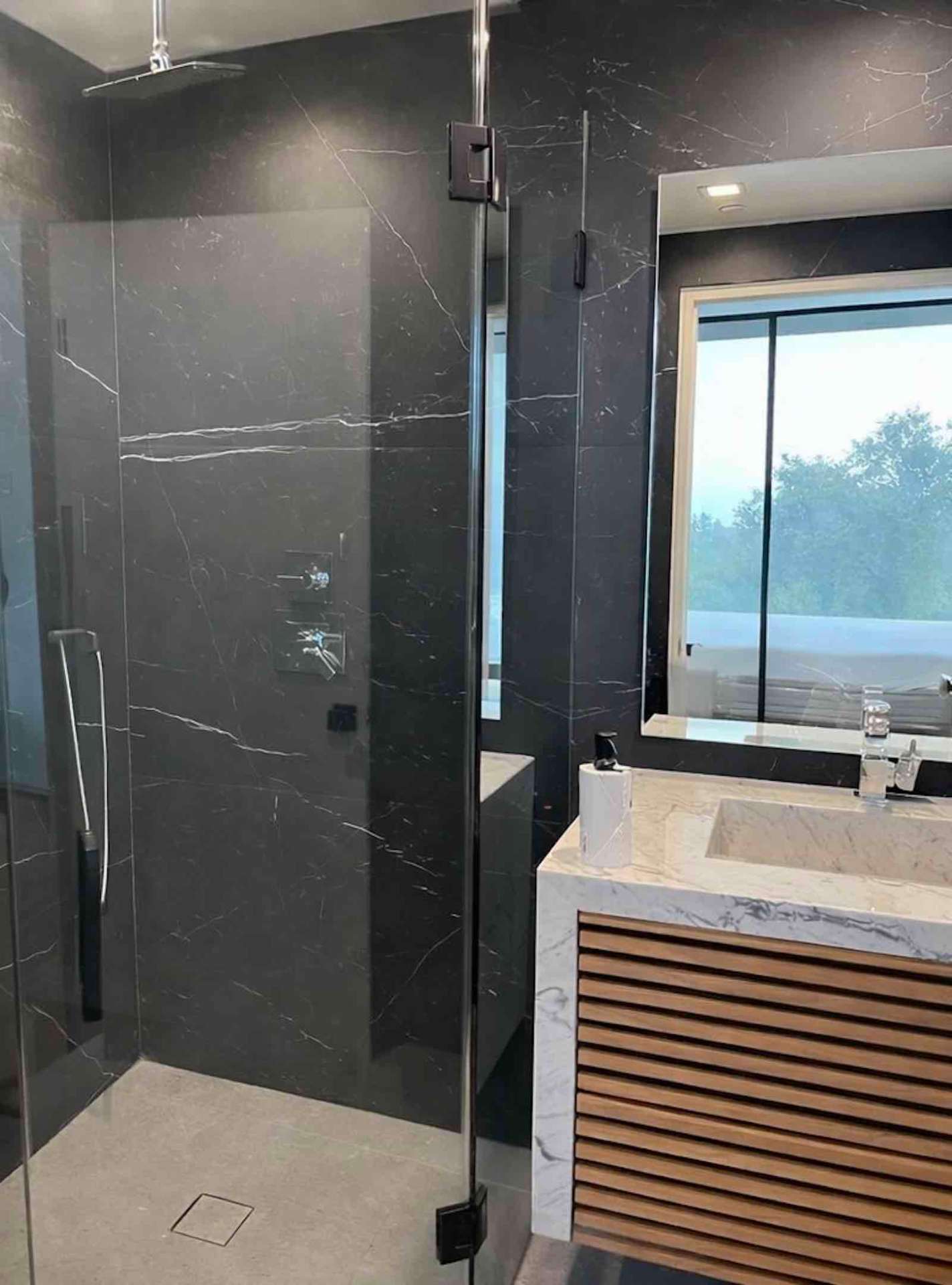 Mulholland Drive black marble walk-in shower with rain head, glass enclosure, and slatted wood vanity