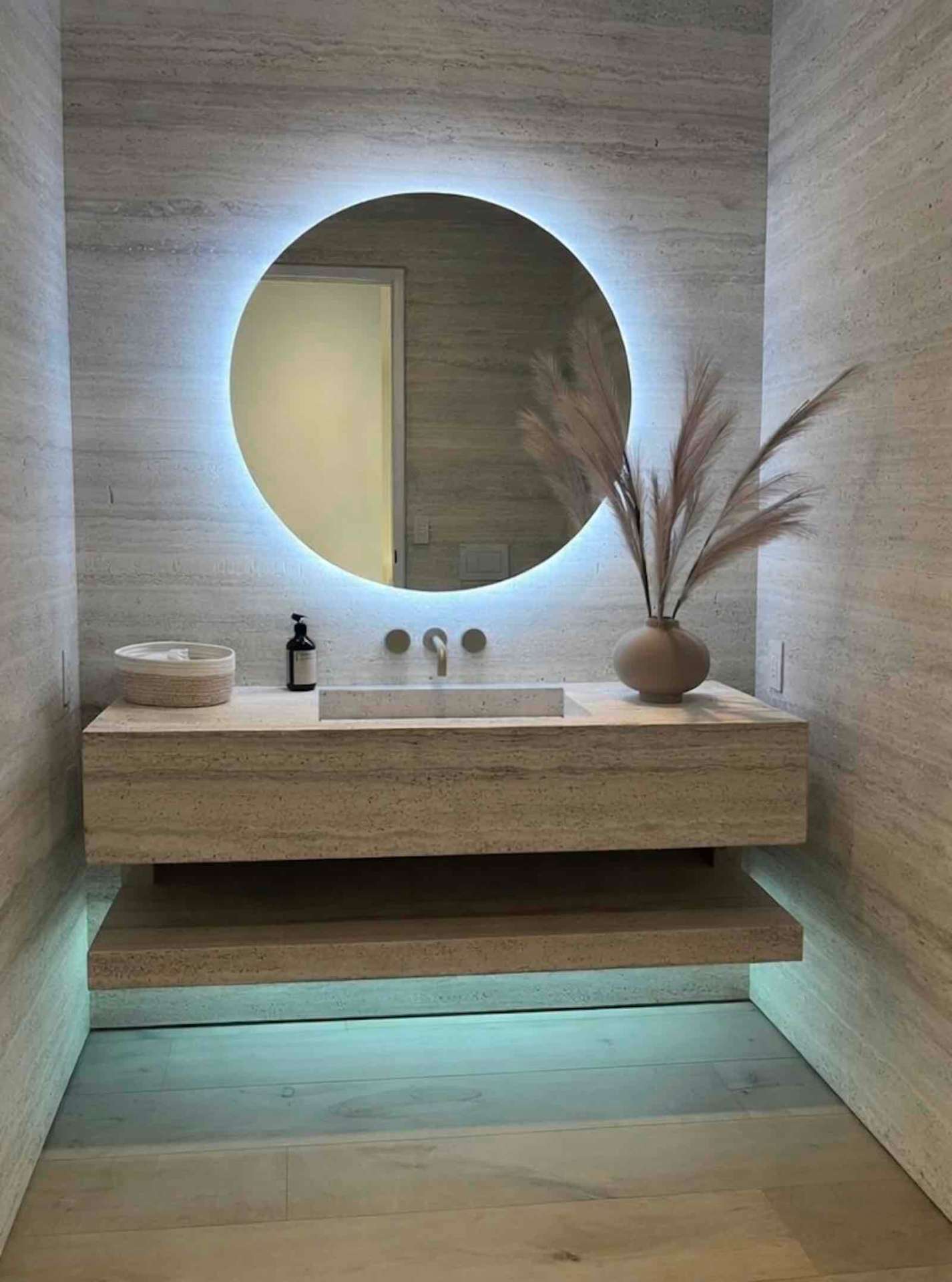 Mulholland Drive powder room with travertine walls, backlit round mirror, and floating stone vanity