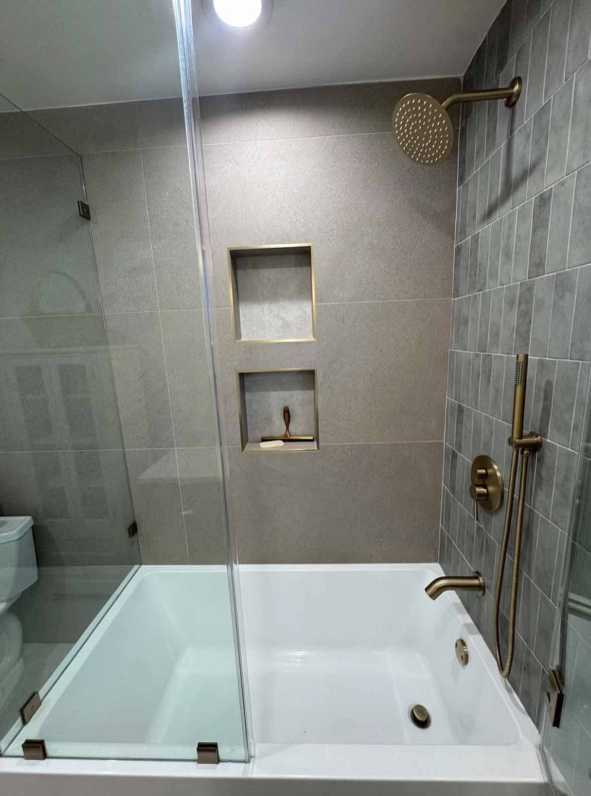 Pasadena bathroom with soaking tub, gray tile walls, brass shower fixtures, and glass panel