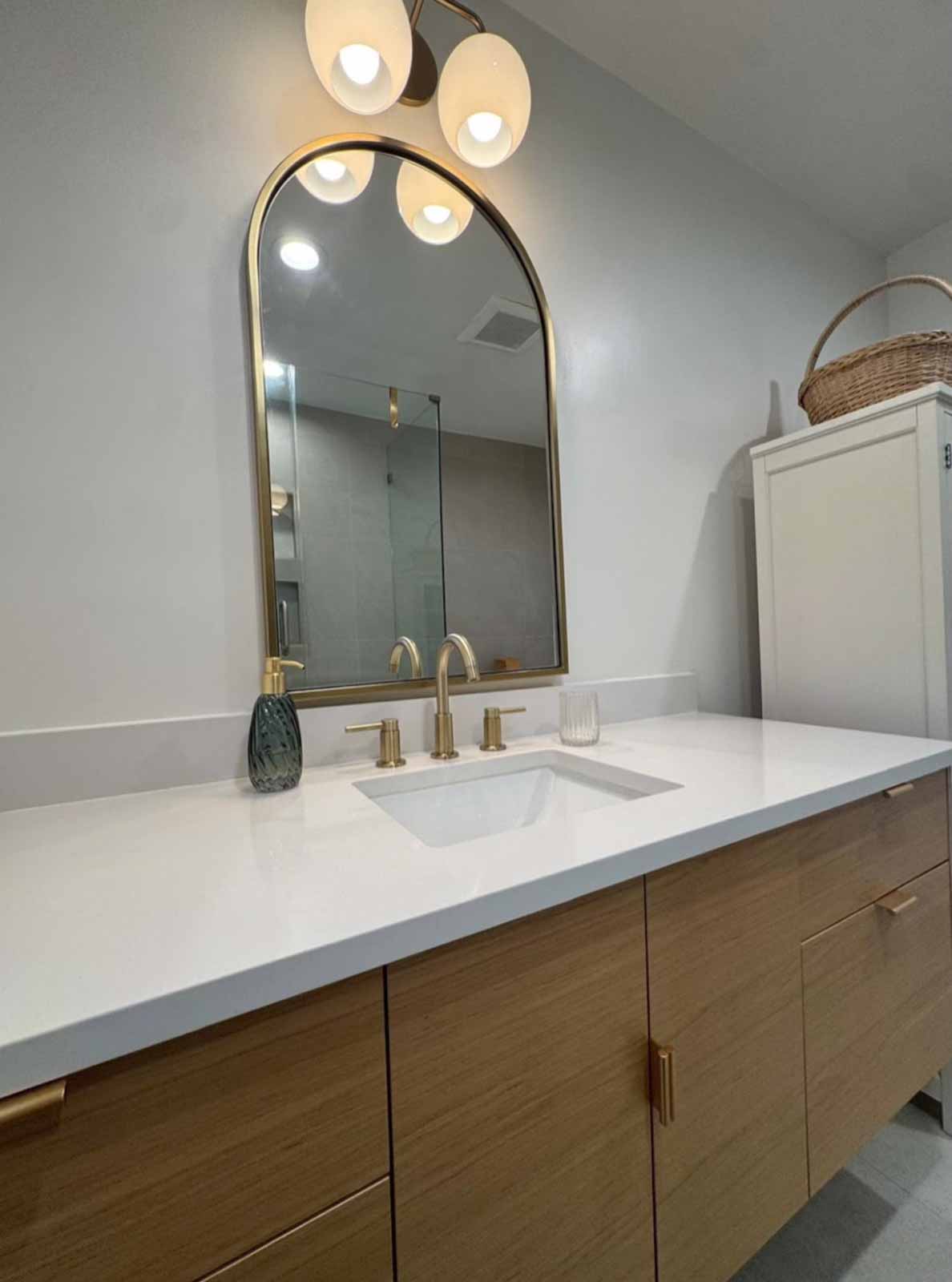 Oak floating vanity with white countertop, arch mirror, and globe light fixture - Pasadena