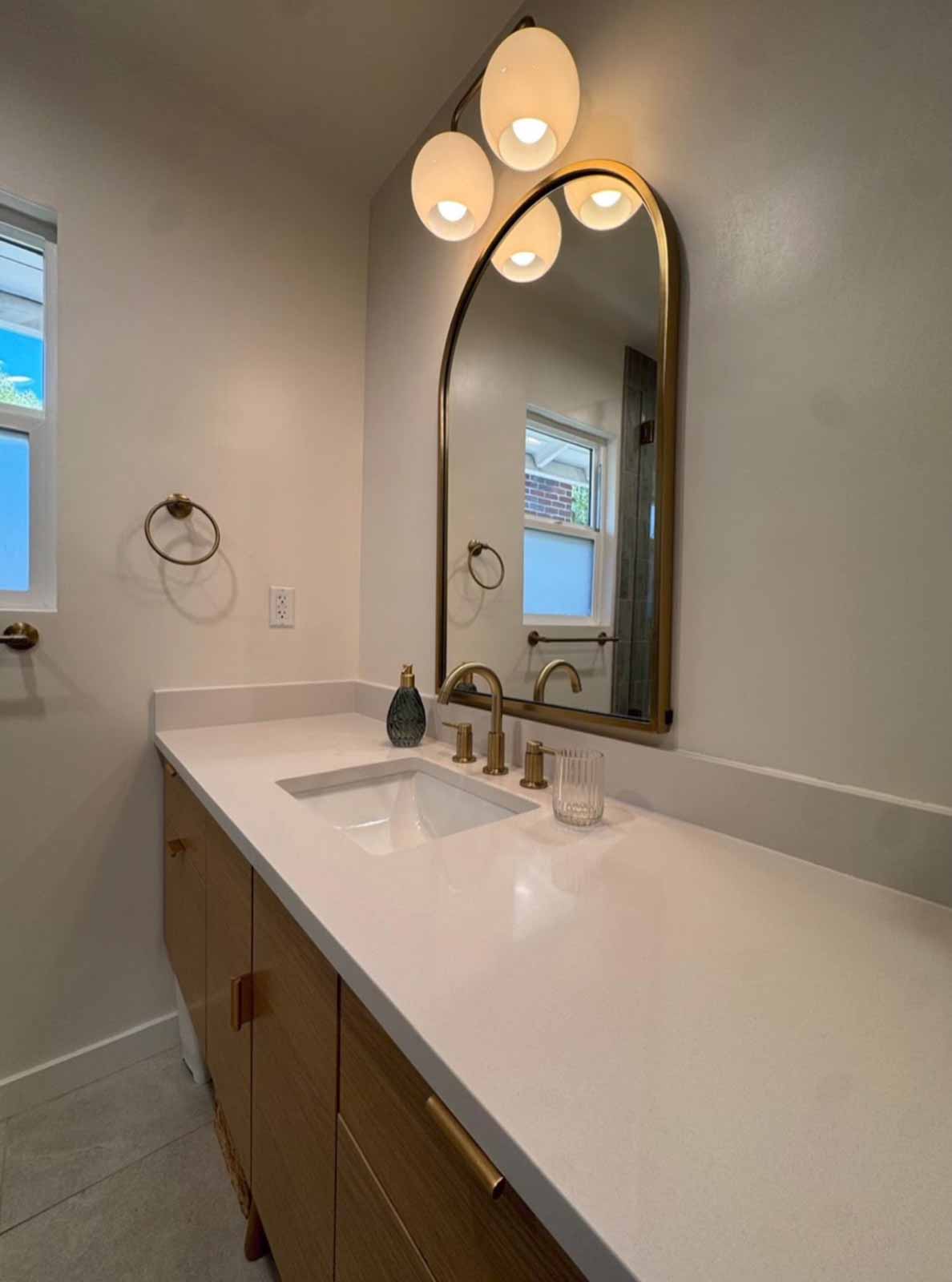 Pasadena vanity detail with brass faucet, arch mirror, and elegant lighting