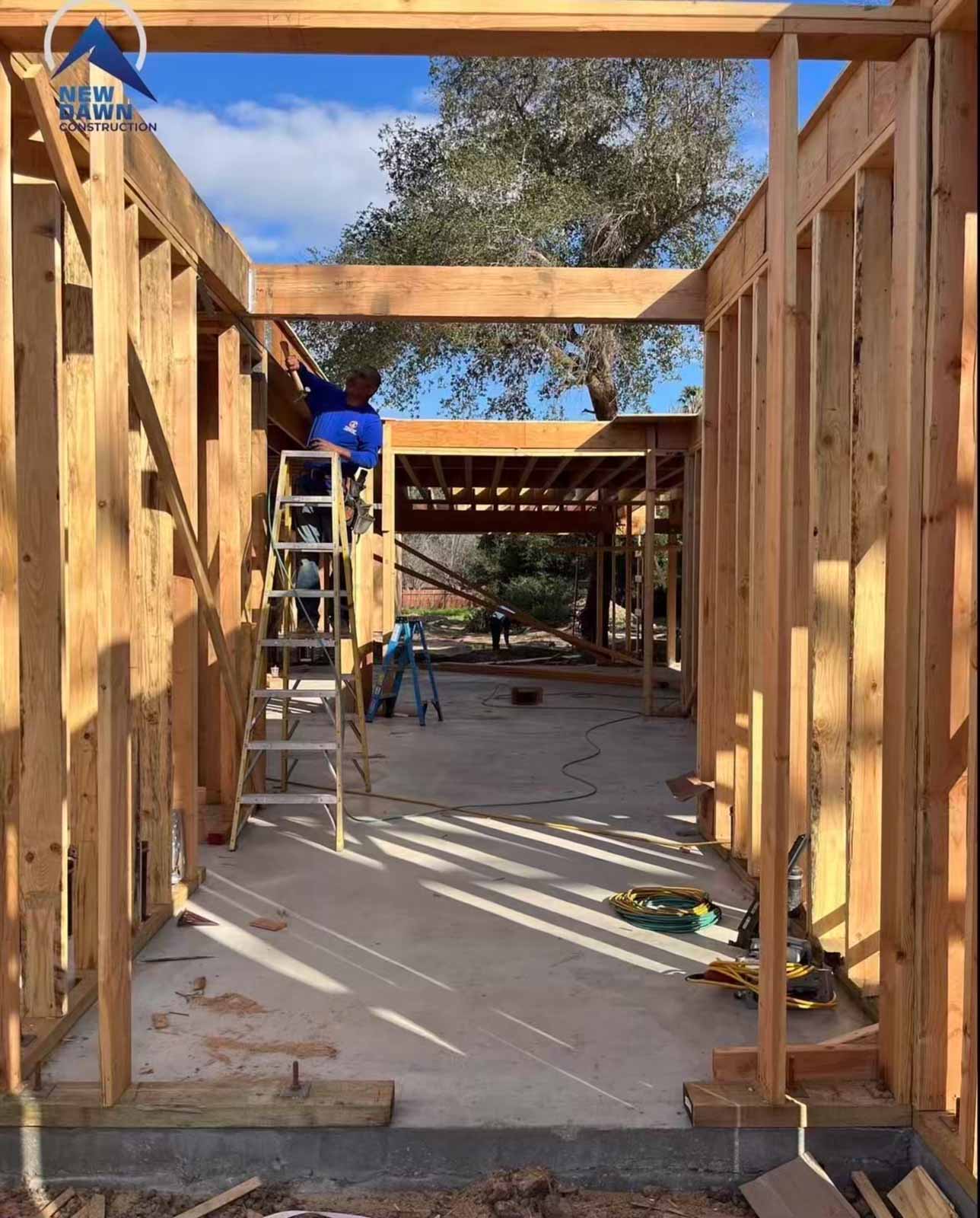 Room addition framing interior view with worker on ladder installing headers - Burbank home expansion