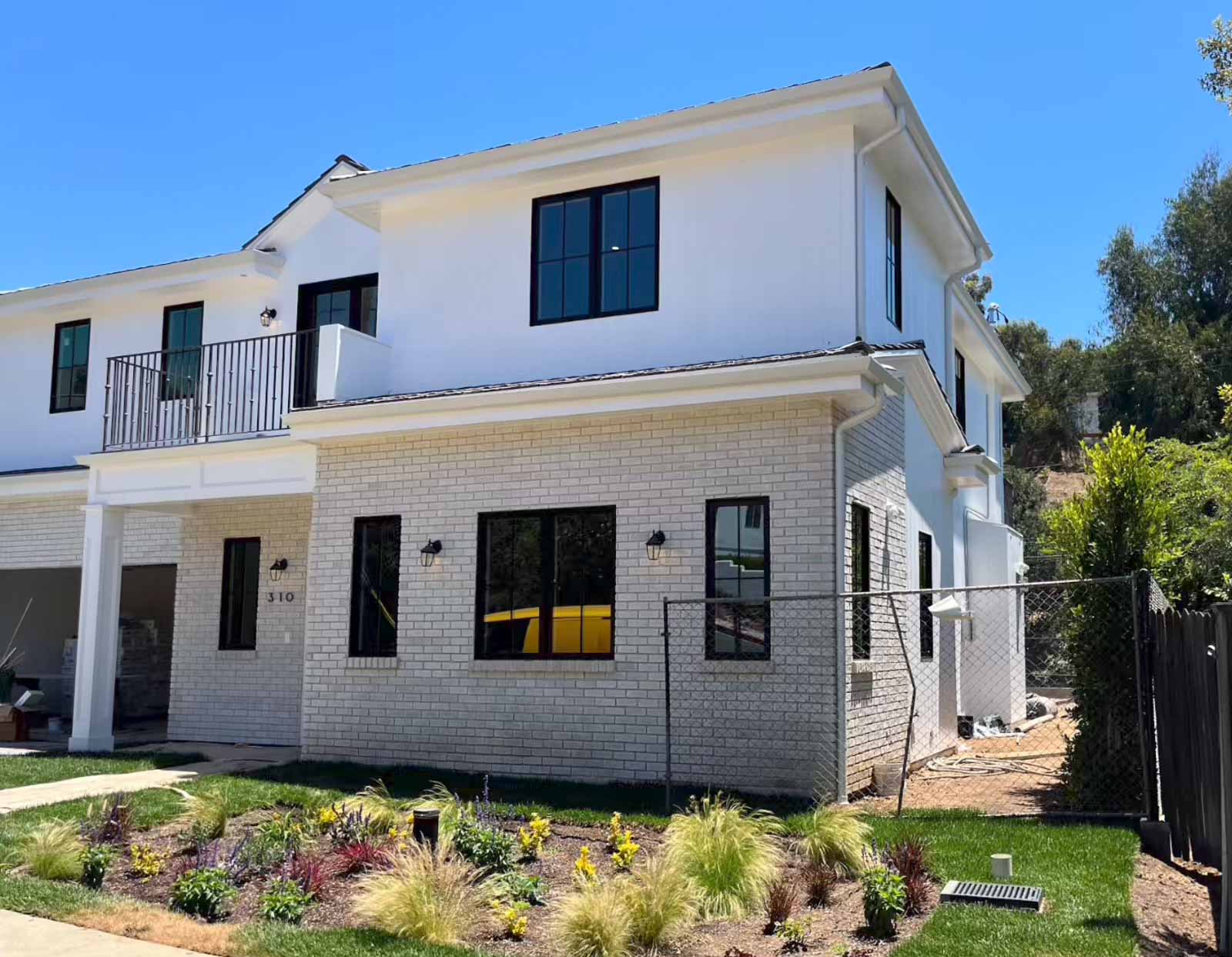 Completed room addition Pasadena with white brick exterior, second story balcony, and landscaped yard - professional home expansion